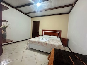 A bedroom with a bed, a nightstand, a wooden door, and a tiled floor.