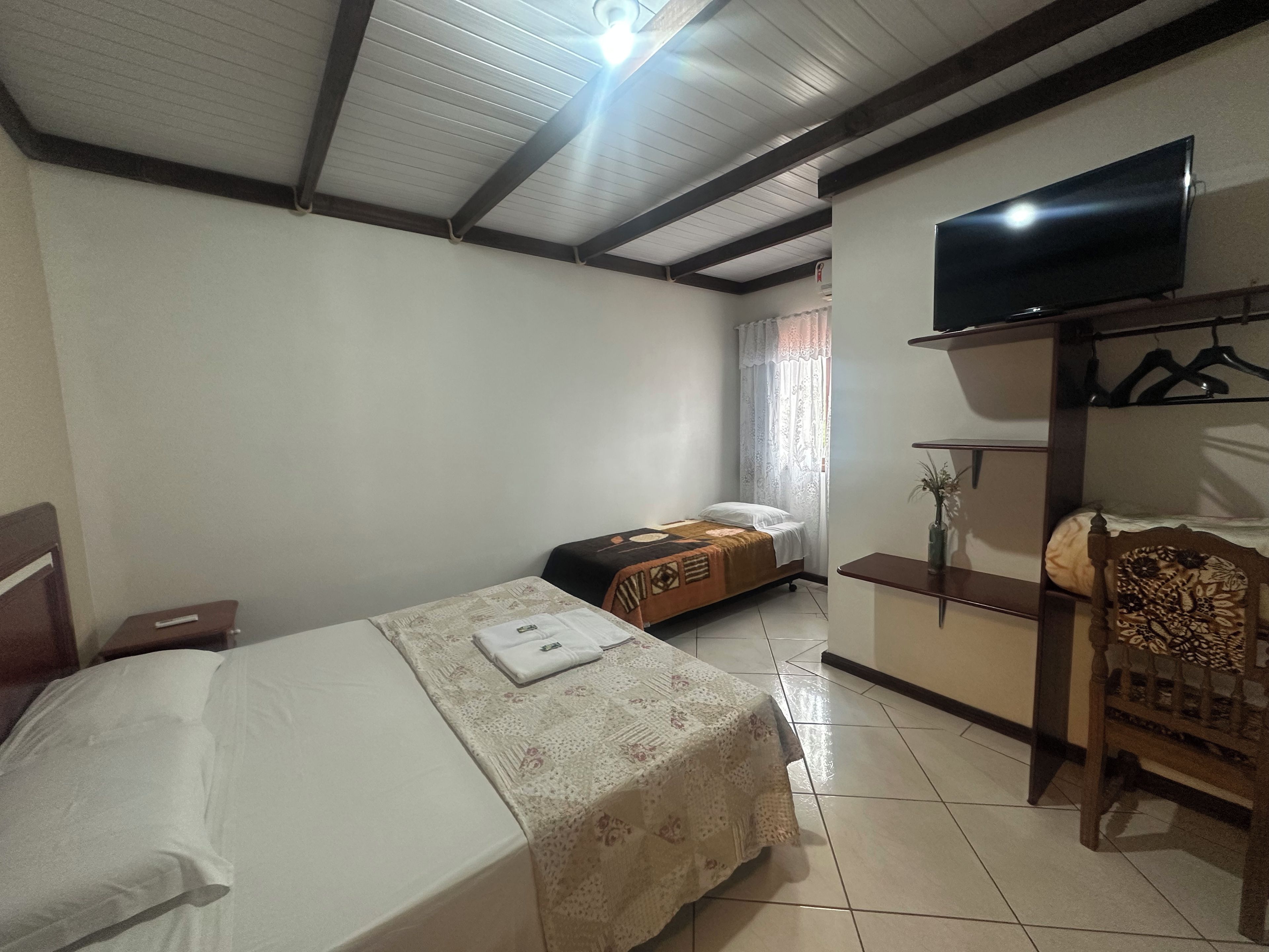 Una habitación de hotel con una cama, una mesita de noche, un televisor sobre un mueble, un armario y una silla.