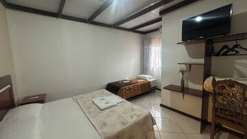 Una habitación de hotel con una cama, una mesita de noche, un televisor sobre un mueble, un armario y una silla.