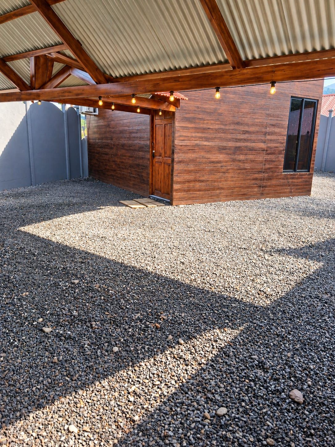 Un espacio al aire libre cubierto con una puerta de madera, suelo de grava y luces colgantes.