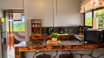A kitchen with a large island, bar stools, a refrigerator, and a view of greenery outside.