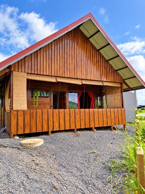 A wooden cabin with a sloped roof, a gravel driveway, and a view of the landscape.