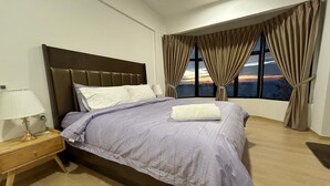 A bedroom with a bed, nightstand, lamp, and a view of the city through large windows.