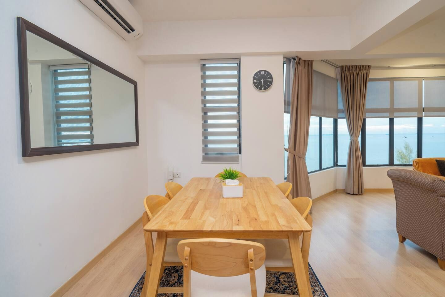 Una sala de estar moderna con una mesa de comedor de madera, un sofá y un amplio ventanal con vista al mar.