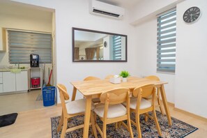 A dining area with a wooden table and chairs, a mirror on the wall, and a clock.