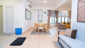A modern living room with a sofa, a dining table with chairs, and a large window with curtains.