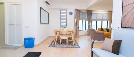 Un salon moderne avec un canapé, une table à manger et des chaises, ainsi qu’une grande fenêtre avec des rideaux.