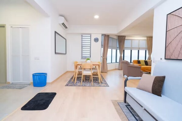 A modern living room with a sofa, a dining table with chairs, and a large window with curtains.