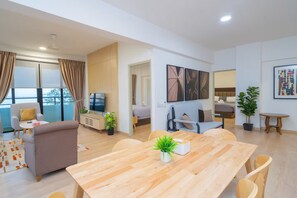 A modern living room with a wooden dining table, a sofa, a TV, and a balcony with curtains.