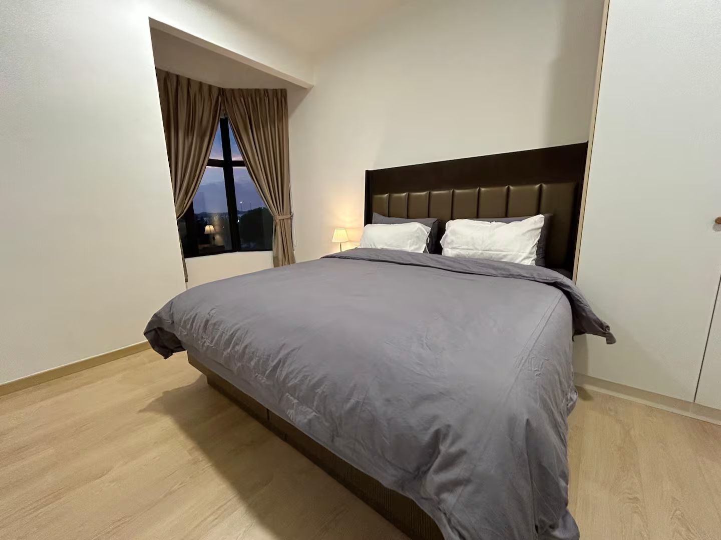 Un dormitorio moderno con una cama grande, una ventana con cortinas y una mesita de noche.