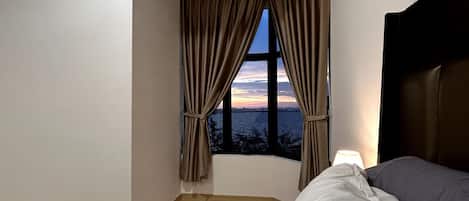 A hotel room with a large window, two beds, a nightstand, and a lamp.