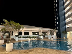 A hotel with a swimming pool, outdoor seating, and a multi-story building.