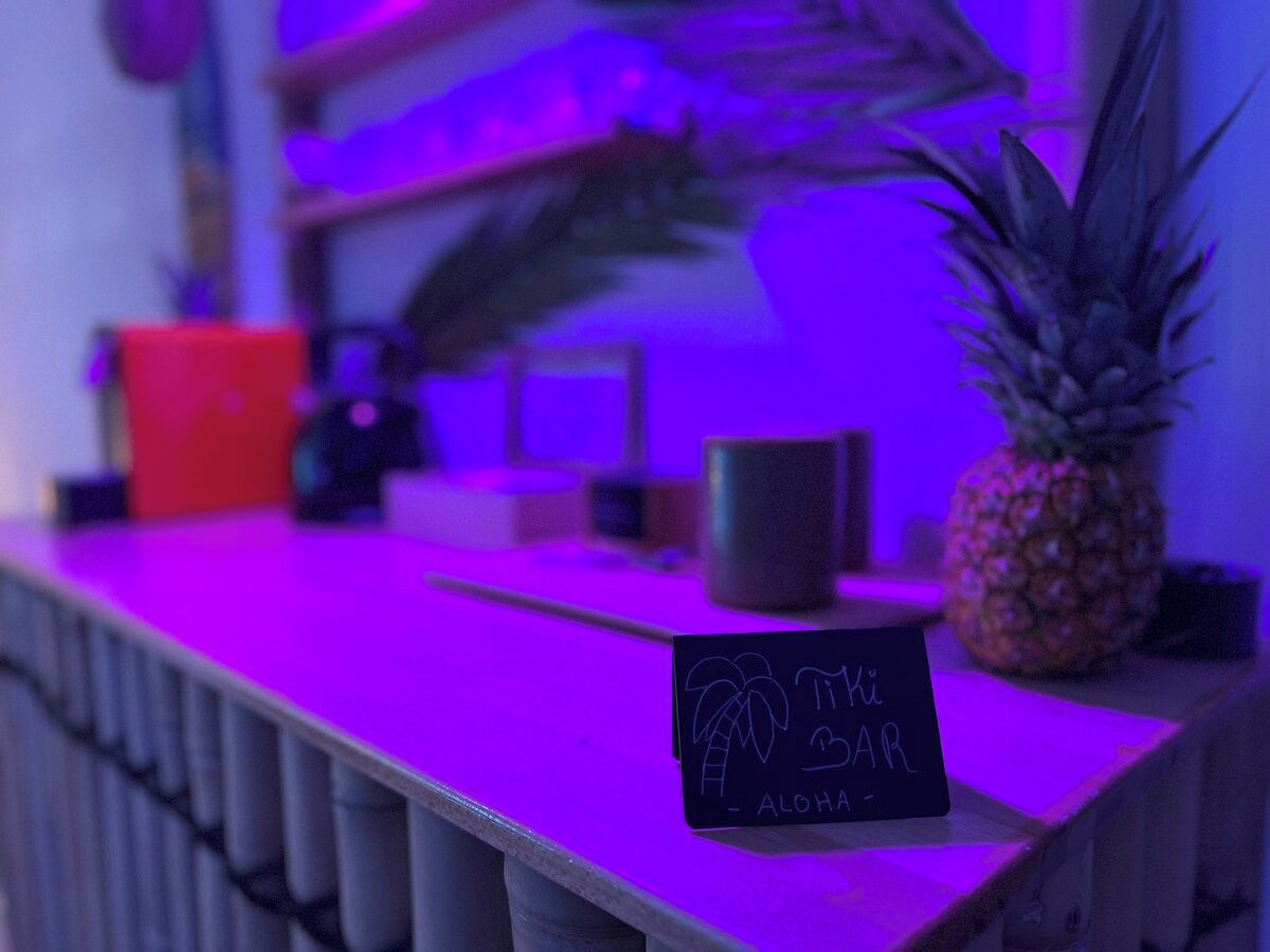 Eine Bartheke mit einem Schild, das 'Tiki Bar - Aloha' zeigt, einer Ananas und einem roten Eimer.