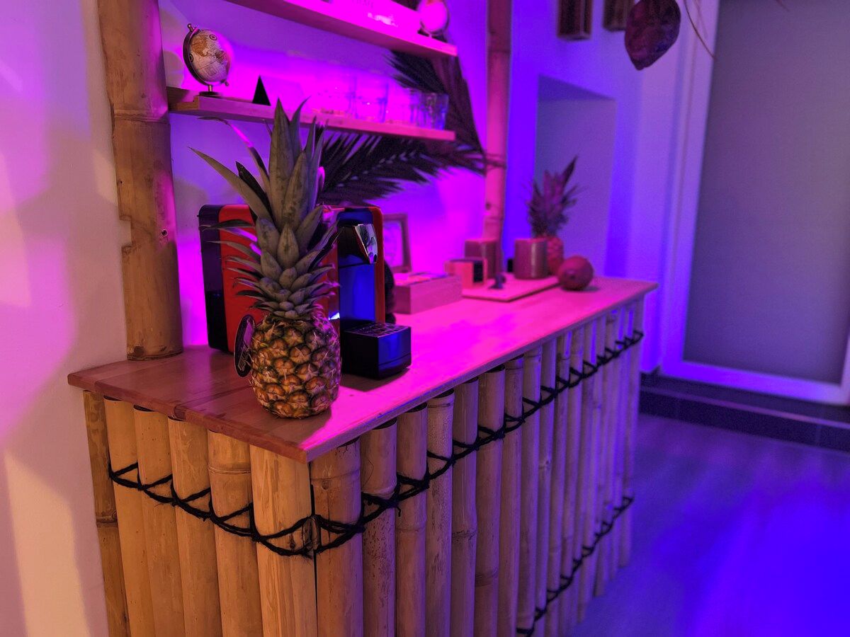 Eine Bar mit Holzausstattung, deren Mittelpunkt eine Ananas bildet, sowie eine kleine Ablage mit Dekoration und ein Wandregal mit einem Globus und weiteren Objekten.