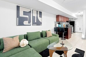 A modern living room with a green sofa, a glass coffee table, and abstract wall art. - A Cozy Boho Oasis | 1BR Center City Philly (Philadelphia)
