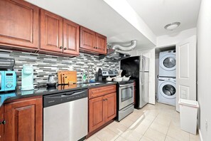 A modern kitchen with wooden cabinets, a stainless steel dishwasher, an oven, a built-in microwave, and a washing machine in the adjacent laundry room. - A Cozy Boho Oasis | 1BR Center City Philly (Philadelphia)