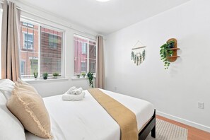 Ein Hotelzimmer mit einem Bett, einem Fenster mit Jalousien, einem an der Wand befestigten Pflanzenregal und einem Wandbild.