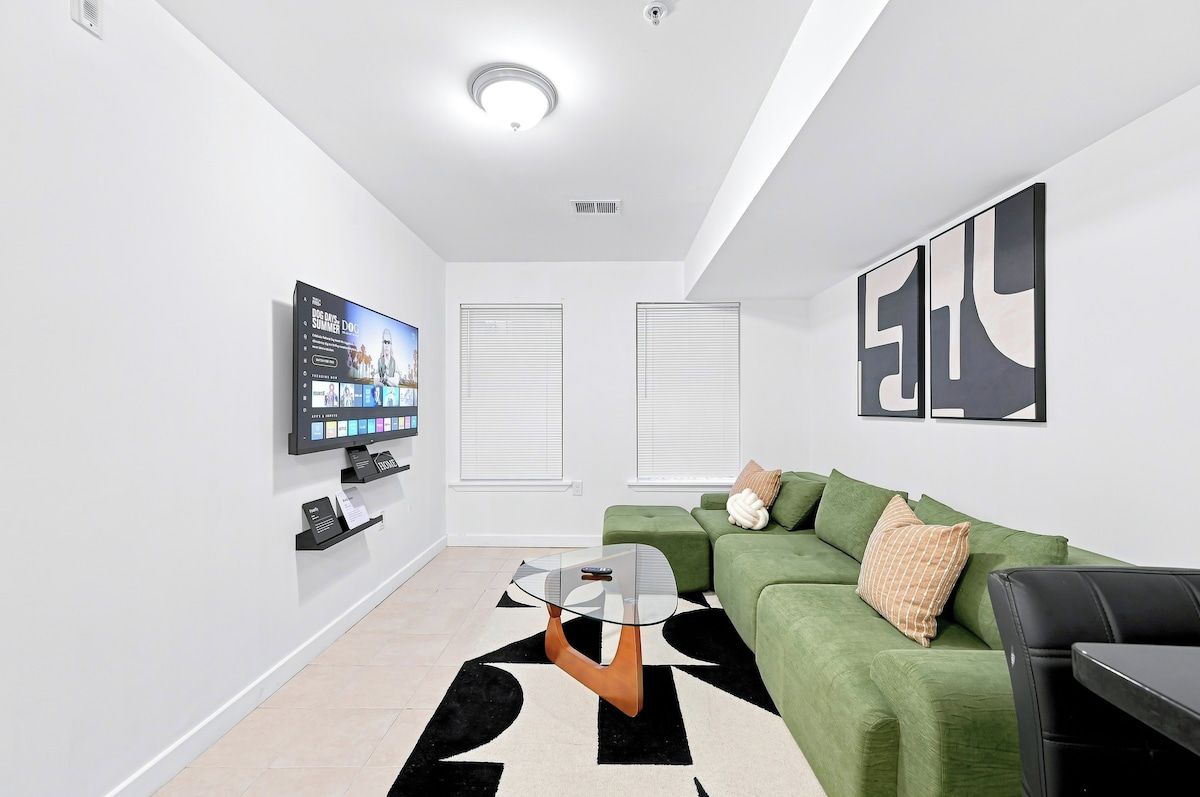 Un salon moderne avec un téléviseur à écran plat, un canapé vert, une table basse en verre et un tapis noir et blanc.