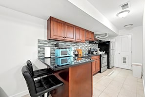 A kitchen with wooden cabinets, a black countertop, and a microwave. - A Cozy Boho Oasis | 1BR Center City Philly (Philadelphia)