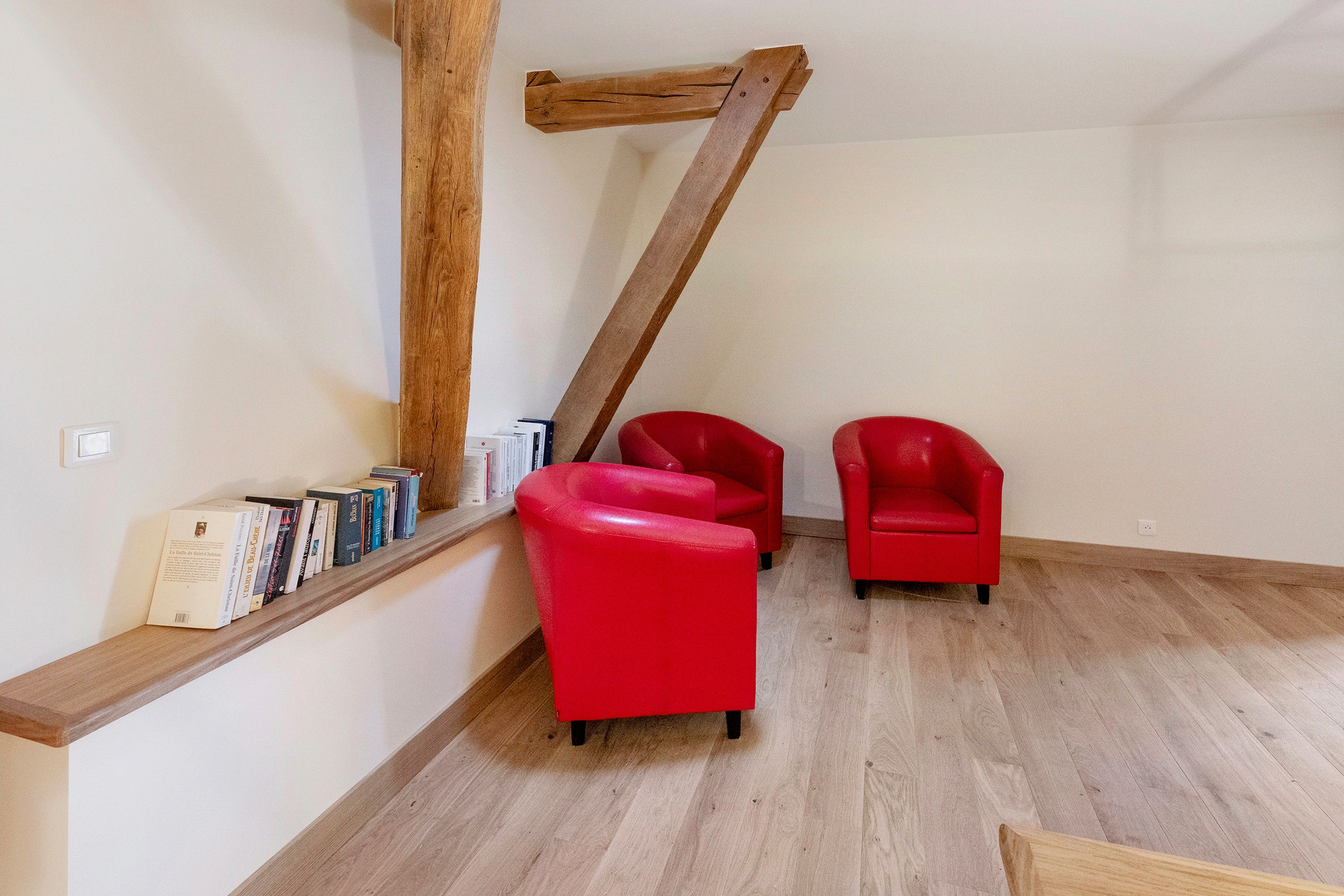 Een kamer met houten balken, een rode stoel en een boekenkast vol boeken.