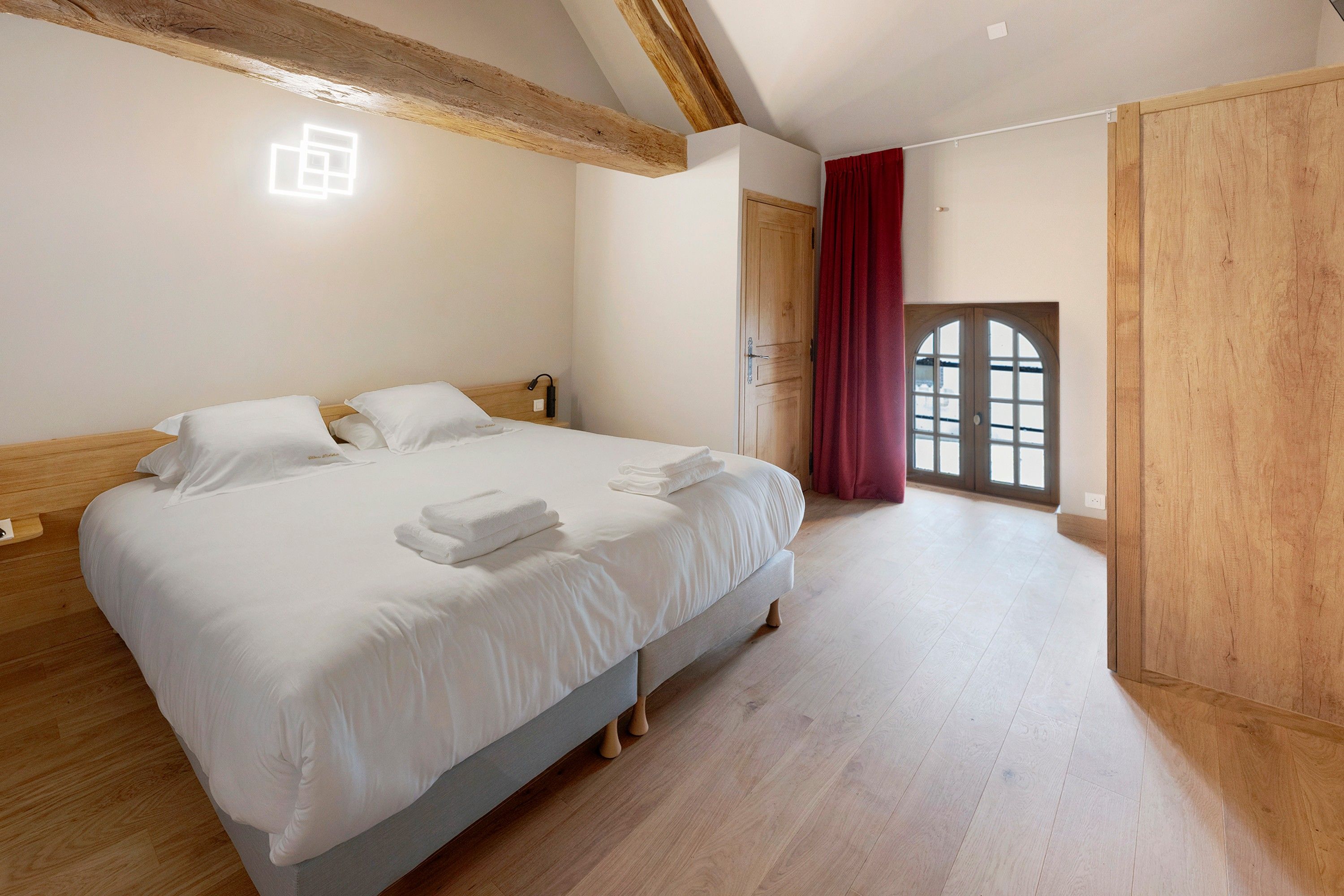 Une chambre d’hôtel avec un grand lit, des poutres apparentes au plafond, une armoire en bois et une fenêtre donnant sur un beau paysage.