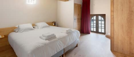 Une chambre d’hôtel avec un grand lit, des poutres apparentes au plafond, une armoire en bois et une fenêtre donnant sur un beau paysage.