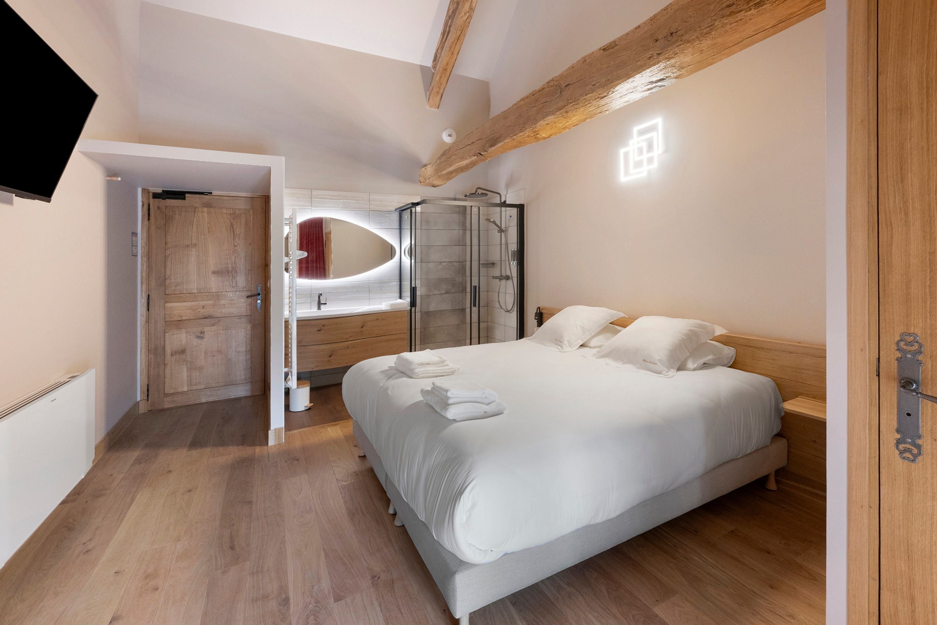 A bedroom with a bed, a walk-in closet, a shower area, and a television mounted on the wall.