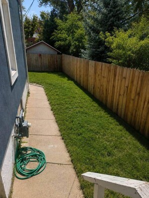 A backyard with a wooden fence, a concrete pathway, and a green hose coiled on the ground. - Cheyenne Country Charm (Cheyenne)