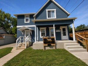 A two-story residential building with a front porch, a mailbox, and a wooden bench. - Cheyenne Country Charm (Cheyenne)