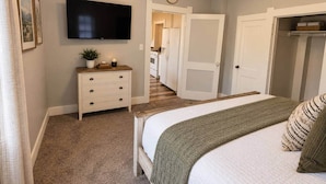 Un dormitorio con cama, cómoda, televisor y pasillo que conduce a otra habitación.