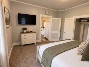 A bedroom with a bed, a dresser, a television, and a hallway leading to another room. - Cheyenne Country Charm (Cheyenne)