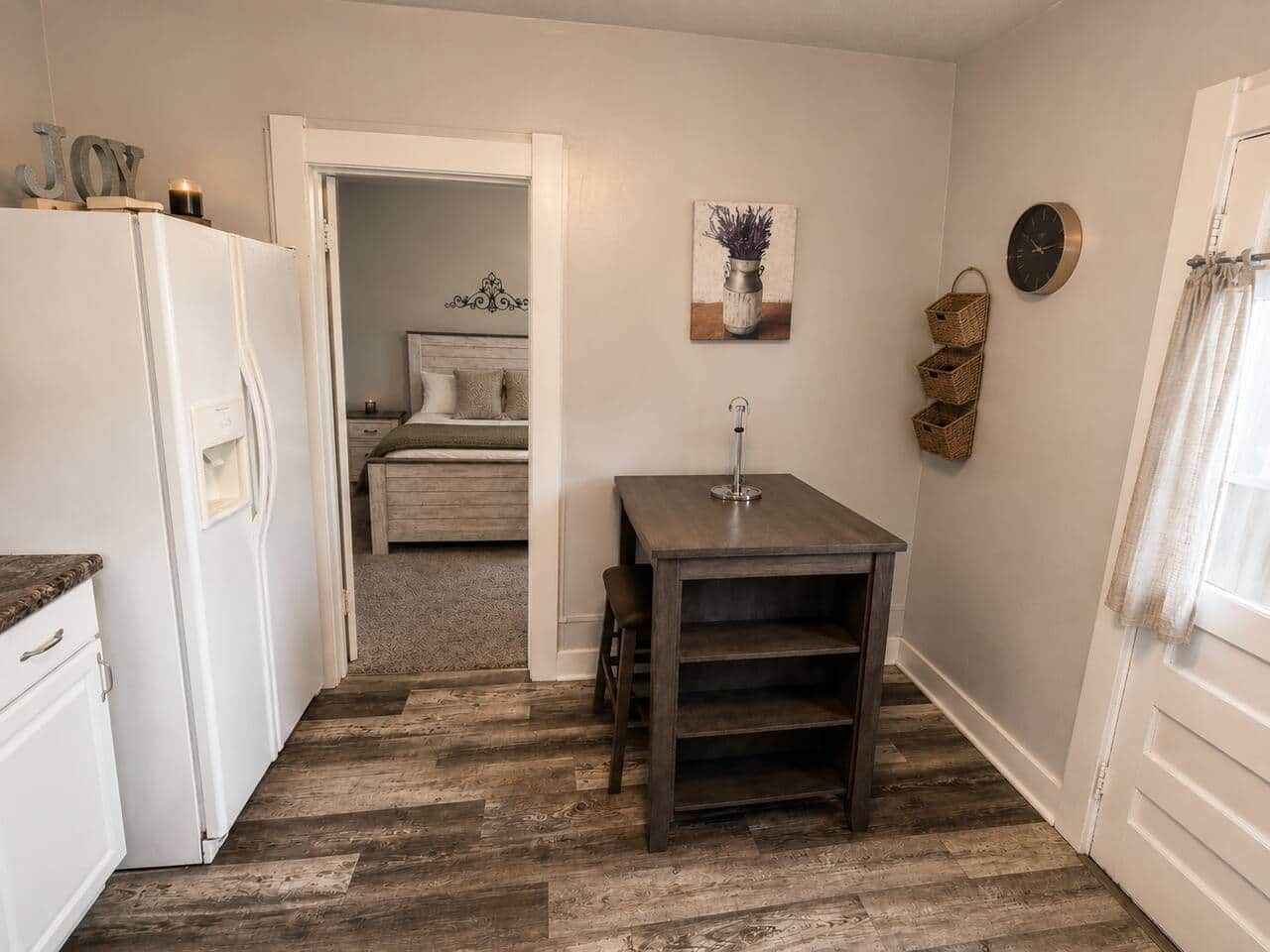 Une petite cuisine équipée d’un réfrigérateur, d’une table en bois et d’un lit dans la pièce adjacente.