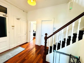 A hallway with wooden flooring, white doors, and a staircase with white balusters. - Spacious 4-Bed Duplex with Pool Table, Near GLA Airport (Renfrewshire)