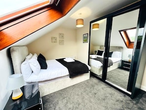 A bedroom with a bed, bedside table, lamp, and a large mirror. - Spacious 4-Bed Duplex with Pool Table, Near GLA Airport (Renfrewshire)