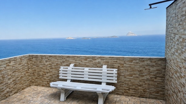 Un banco blanco en un espacio al aire libre con muros de piedra y vista al mar y a islas distantes.