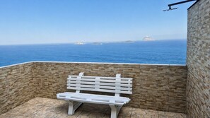 Eine weiße Bank in einer von Steinmauern umgebenen Außenanlage mit Blick auf das Meer und ferne Inseln.