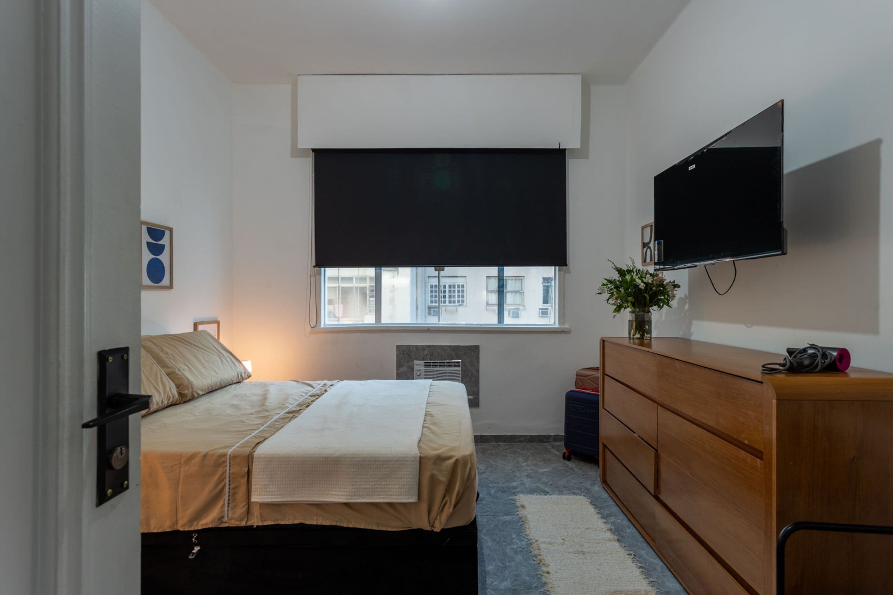 A bedroom with a bed, a dresser, a television, and a window with blinds.