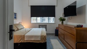 Un dormitorio con cama, cómoda, televisor y ventana con persianas.