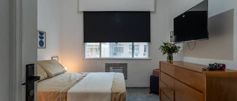 A bedroom with a bed, a dresser, a television, and a window with blinds.
