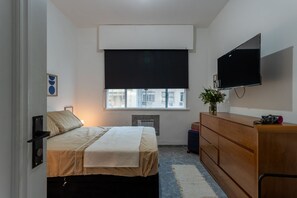 A bedroom with a bed, a dresser, a television, and a window with blinds. - Apto Beira-mar com Ar Condicionado em Copacabana (Rio de Janeiro)