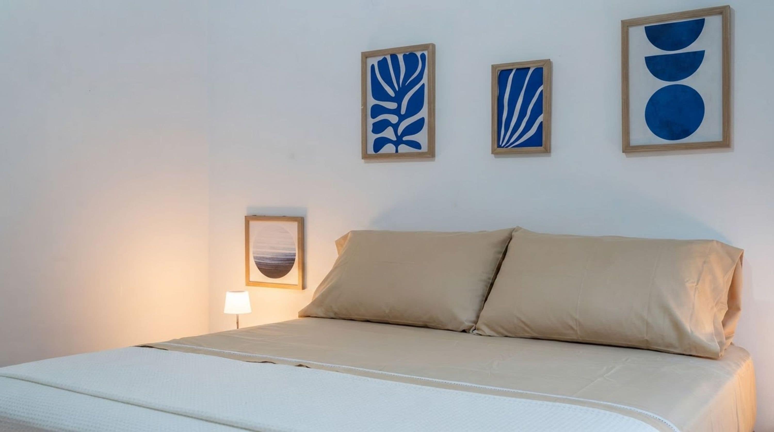 A bedroom with a bed, a nightstand, a lamp, and three wall art pieces.