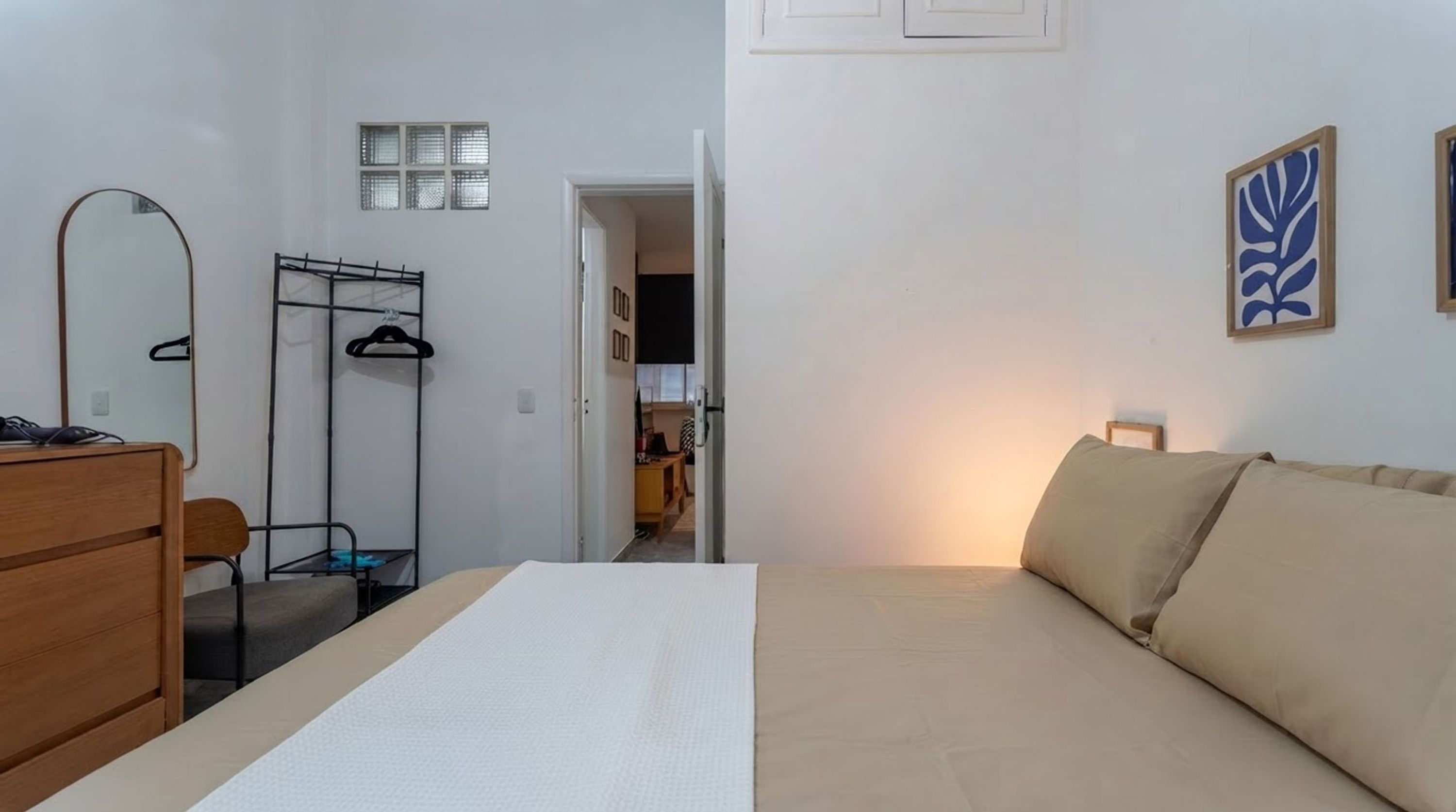 A bedroom with a bed, a dresser, a mirror, a coat rack, and a door leading to a bathroom.
