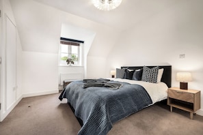A bedroom with a bed, bedside table, lamp, and a window with a view.