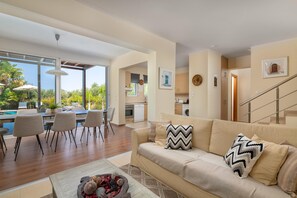 A modern living room with a sofa, a dining area with chairs, a kitchen in the background, and a staircase. - Villa Olvia in Rhodes (Rhodes)