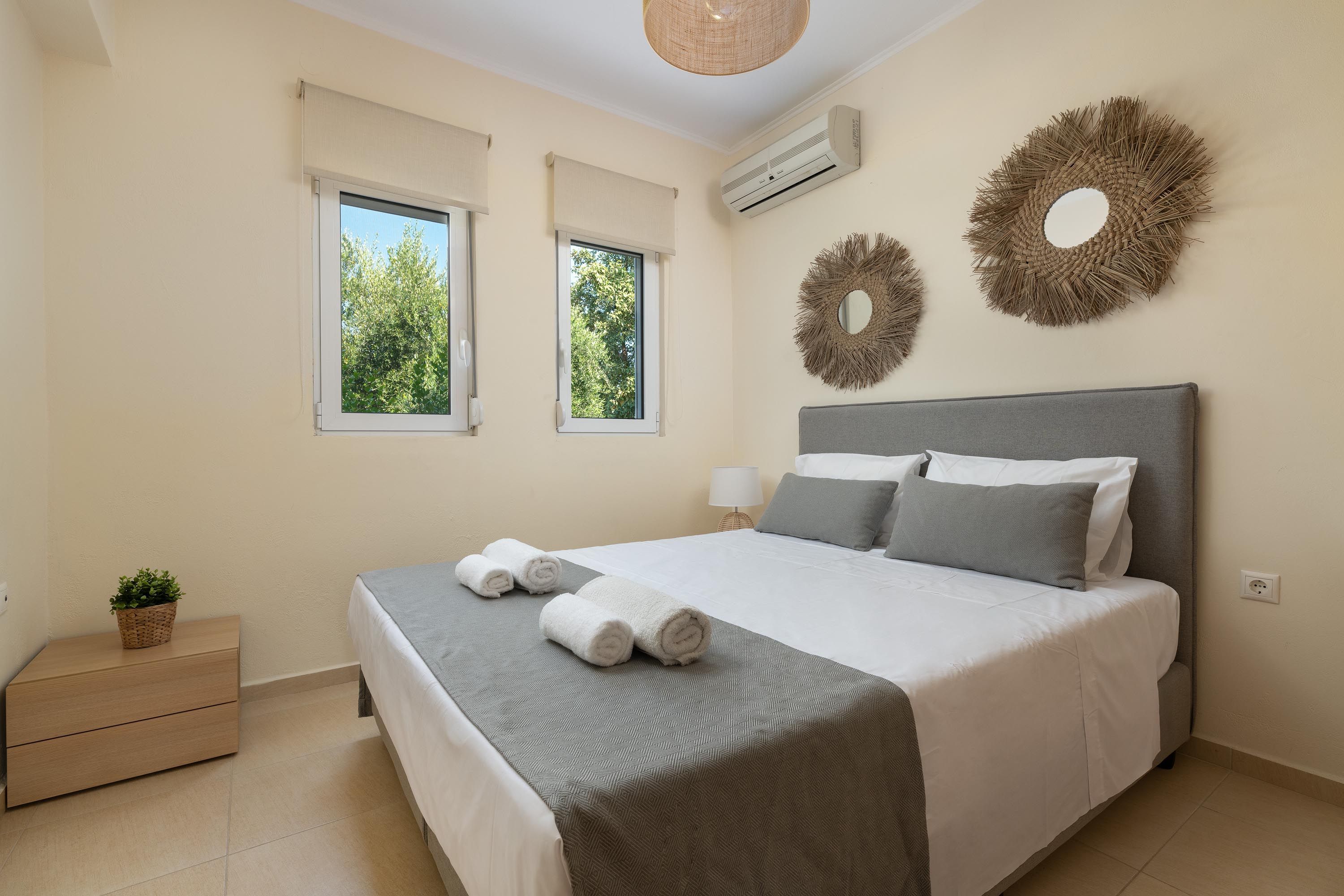 A bedroom with a bed, two windows, an air conditioner, and decorative wall hangings.