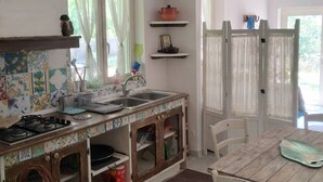 A kitchen with a gas stove, a sink, and a dining table with chairs. There are shelves above the counter and a basket on the floor. - Selvaluna . (Campania)