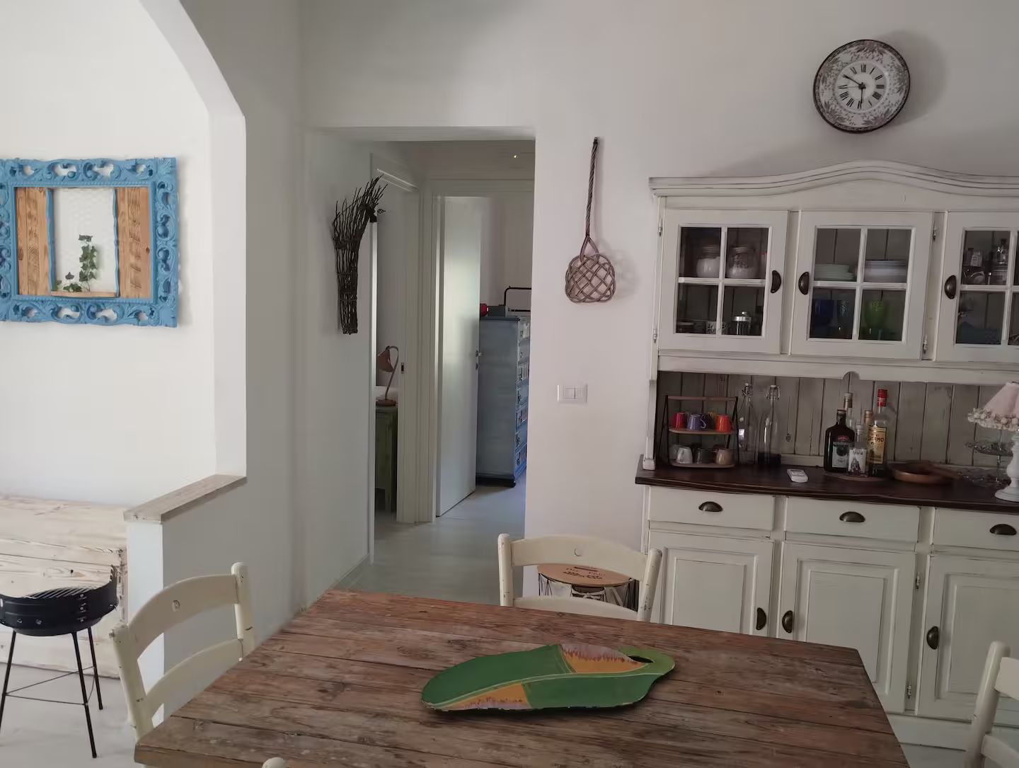 A kitchen with white cabinets, a wooden table, and a hanging clock.
