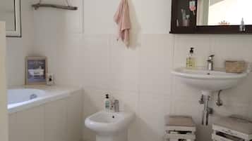 Ein Badezimmer mit Badewanne, Bidet und Waschbecken. An den Wänden befinden sich Dekorationen und ein Spiegel über dem Waschbecken.