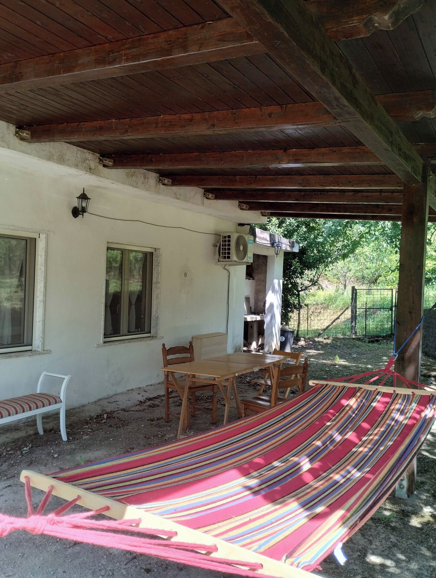 A covered outdoor area with a wooden table and chairs, a hammock, and a window.