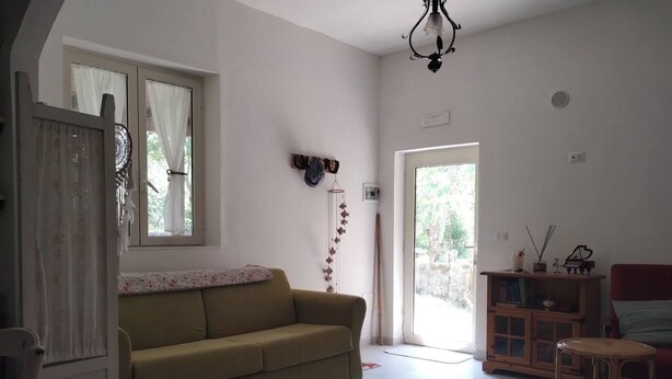 A living room with a sofa, a coffee table, a wooden cabinet, and a door leading outside. - Selvaluna . (Campania)